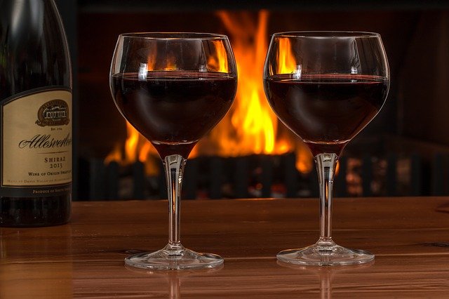 Dvě sklenky červeného vína, v pozadí hořící krb